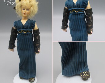May include: A porcelain doll wearing a teal blue dress with black lace sleeves and gold trim. The doll has blonde hair and is wearing gold shoes with black polka dots.