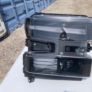 May include: A black and clear automotive headlight assembly. The headlight has a rectangular shape with multiple light elements and a clear lens. The assembly is designed for a vehicle and is likely an aftermarket or replacement part.