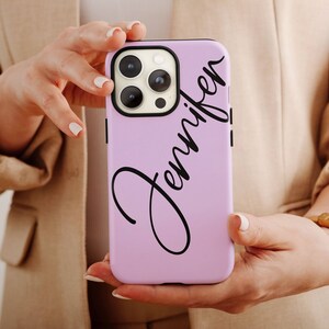 May include: A light purple smartphone case featuring the name Jennifer written in a black cursive script font. The case has a black camera lens cutout area and covers the back of a smartphone with a triple camera system.