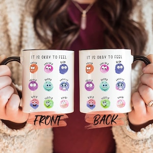 May include: White ceramic mug with a black handle. The mug has a watercolor design of different emotions with the text "It is okay to feel" on the front and back.
