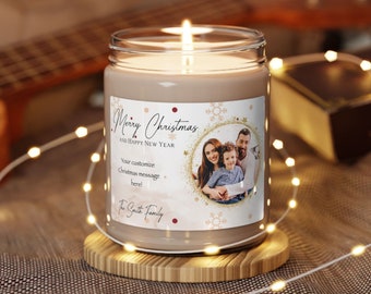 May include: A lit, beige-colored candle in a glass jar with a label that reads "Merry Christmas and Happy New Year." The label includes a family photo and space for a custom message. The candle sits on a wooden coaster, with string lights and a guitar in the background.