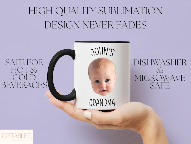 A hand holding a white mug with a black handle, featuring a photo of a baby's face.