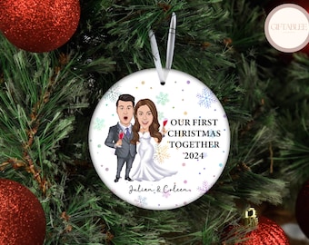 Może przedstawiać: Biała, okrągła ozdoba choinkowa z ilustracją pary z kreskówek, trzymającej kieliszki do wina. Tekst brzmi "OUR FIRST CHRISTMAS TOGETHER 2024" z imionami "Julian & Coleen" poniżej. Ozdoba zawieszona jest na białej wstążce.