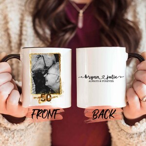 May include: White ceramic mug with a black handle. The front of the mug features a black and white photo of a couple with a gold 50th anniversary design. The back of the mug has the text "Bryan & Julie Always & Forever" in black.