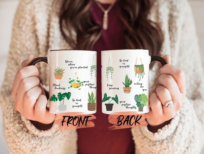 May include: White ceramic mug with a black handle. The mug has a green and yellow plant design with inspirational quotes. The front of the mug says "bloom where you're planted, plant kindness, grow positive thoug, be leaf in yourself". The back of the mug says "be leaf in yourself, keep growing, rooting for you, grow positive thoughts".