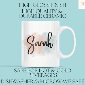 Op de afbeelding: Een witte keramische mok met een aquarelontwerp in tinten perzik en blauw. De mok heeft een zwart handvat en de naam "Sarah" staat in zwarte cursieve letters op de voorkant. De mok is vaatwasser- en magnetronbestendig.
