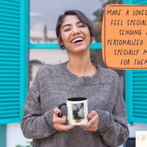 May include: A woman is holding a white mug with a black handle. The mug has a photo printed on it. The text on the mug says "50". The woman is smiling and looking at the camera. The background is a blue wall with white shutters.