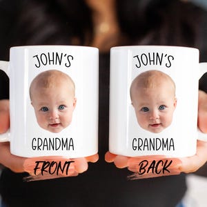A person is holding two white mugs with a baby's face printed on them.