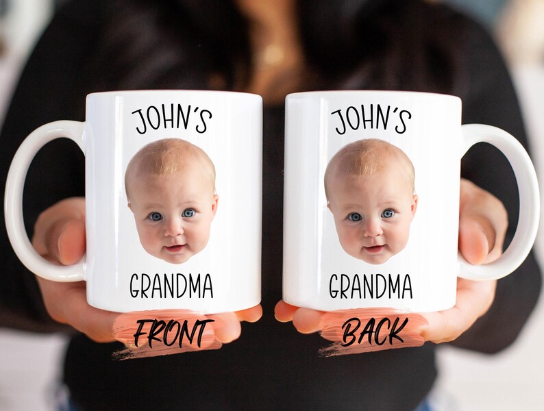 A person is holding two white mugs with a baby's face printed on them.