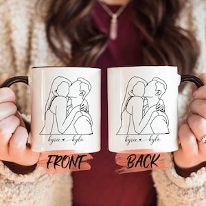 Könnte beinhalten: Weiße Keramiktasse mit schwarzem Henkel. Die Tasse zeigt eine Linienzeichnung eines sich umarmenden Paares, mit dem Text "kyrie kyla" unter dem Bild. Die Tasse wird von vorne und hinten gezeigt.