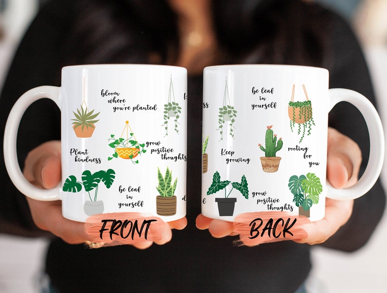 May include: White ceramic mug with a plant theme. The front of the mug features illustrations of various plants with text that reads "Plant kindness", "Bloom where you're planted", "Be leaf in yourself", and "Grow positive thoughts". The back of the mug features similar illustrations and text that reads "Keep growing", "Be leaf in yourself", "Rooting for you", and "Grow positive thoughts".