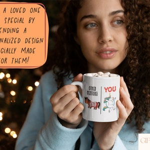 K&ouml;nnte beinhalten: Eine wei&szlig;e Keramiktasse mit einem schwarzen und roten Design. Die Tasse zeigt ein Einhorn und ein Pferd. Der Text auf der Tasse lautet "Other Mentors" und "You".