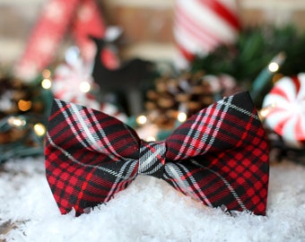 May include: A red, black, and white plaid bow tie. The bow tie is sitting on a bed of white snow.
