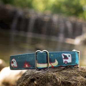 K&ouml;nnte beinhalten: Ein blaues Hundehalsband mit einem Camping-Motiv, das einen Wohnwagen, ein Kanu und ein Lagerfeuer zeigt. Das Halsband hat eine silberne Metallschnalle.