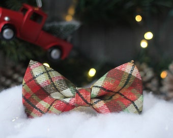May include: A red, green, and gold plaid bow tie. The bow tie is made of fabric and has a festive Christmas feel.