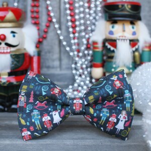 May include: A dark blue bow tie with a festive Nutcracker pattern featuring a variety of characters, musical instruments, and holiday symbols.