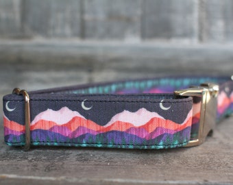 Puede incluir: Un collar de perro negro con un estampado colorido de montañas y luna. El collar tiene una hebilla plateada y un anillo en D dorado.
