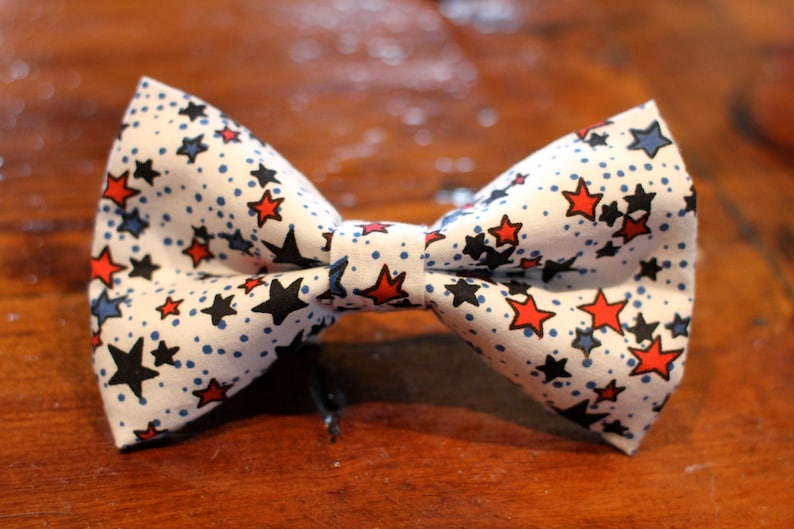 May include: A white bow tie with a red, white, and blue star pattern. The bow tie is made of fabric and has a classic bow tie shape.