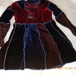 May include: A long-sleeved velvet dress with a patchwork design. The dress is made of different colors of velvet, including red, blue, and brown. The dress has a ruffled hem and a V-neckline.
