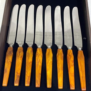 May include: Set of eight vintage butter knives with amber colored handles. The knives are made of stainless steel and have the words "Made in Canada" etched on the blades.