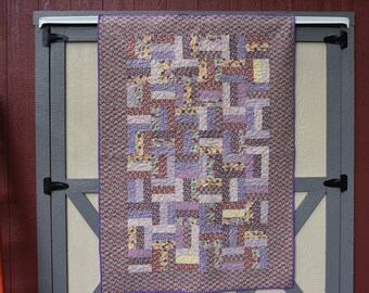 Handmade quilt in various colors of purple, with a purple backing, machine quilted in a geometric pattern