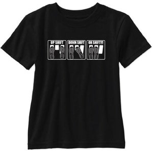 May include: Black t-shirt with a white graphic of three stick figures wearing shoes, representing the car pedals. The text "Up Shift", "Down Shift", and "Oh Shift!!!" is printed above each figure.