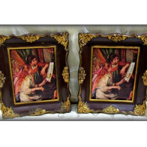 May include: Two ornate gold and brown picture frames with a painting of two women playing a piano. The painting is in a vintage style with warm colors.