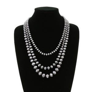 May include: A three-strand pearl necklace with graduated pearls. The necklace is made of black pearls and is displayed on a black velvet bust form.