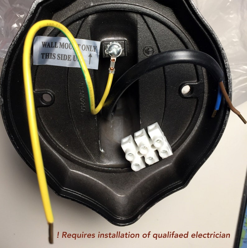 May include: A black electrical fixture's interior with wiring, including yellow and black cables, and a white terminal block. The text "WALL MOUNT ONLY THIS SIDE UP" is visible. Requires installation of a qualified electrician.
