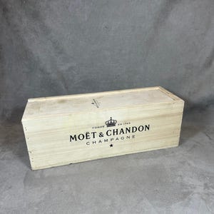 May include: A rectangular wooden box with a lid. The box is light-colored with the words "MOËT & CHANDON CHAMPAGNE" printed in black, along with a crown and star. The box is likely for storing or transporting champagne bottles.