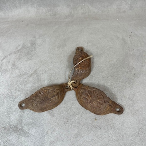 Peut inclure: Trois tirettes de tiroir en fonte rouillée avec des motifs ornés. Les tirettes sont reliées par une ficelle.