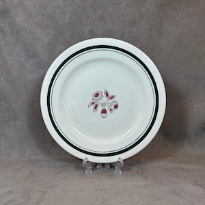 Peut inclure: Assiette en céramique blanche avec un bord noir et un motif floral rouge au centre.
