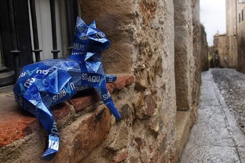 May include: A blue cat sculpture made from recycled materials, sitting on a brick wall. The sculpture is made from blue plastic and has the words "Aquarius" and "Smaqu" printed on it.
