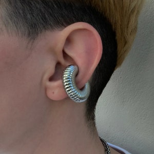 May include: A silver ear cuff with a coiled design. The cuff is worn on the upper part of the ear.