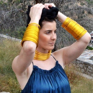 May include: A woman wearing a dark blue dress with a gold necklace and gold bangles on her wrists. She is adjusting her black head scarf.