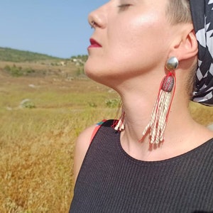 Può includere: Una donna indossa una canotta nera e un foulard a fantasia bianco e nero. Indossa orecchini lunghi e pendenti con perline bianche e filo rosso.