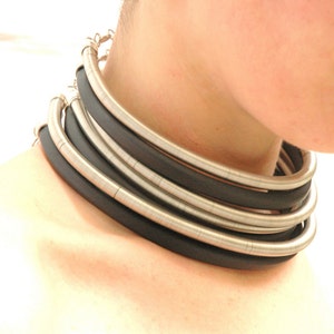 Puede incluir: Un collar choker plateado y negro con múltiples capas de metal y cuero.