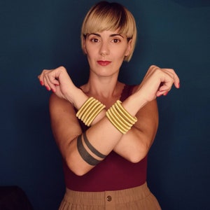 Può includere: Una persona indossa una blusa color granata e una gonna marrone con braccialetti dorati su entrambi i polsi.