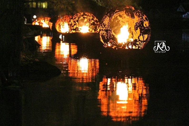 May include: A series of metal fire orbs with intricate designs are floating on a dark body of water. The orbs are lit from within, casting a warm glow on the water's surface.