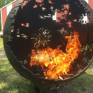 May include: A large metal sphere with a cut-out design resembling the Death Star from Star Wars. The sphere is sitting on a metal base and has a fire burning inside.