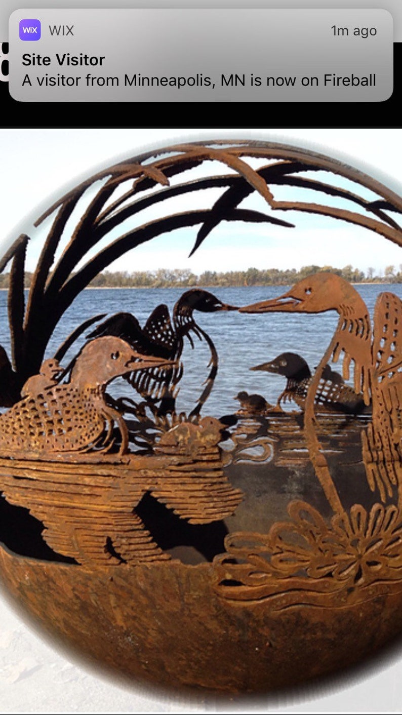 May include: A rusty metal sculpture of a family of loons with their young, set against a backdrop of water and reeds. The sculpture is in the shape of a sphere.