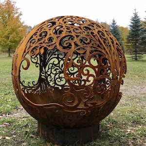 May include: A large, rusty metal sphere with a cut-out design of a tree with intricate branches and leaves. The sphere is sitting on a grassy surface.