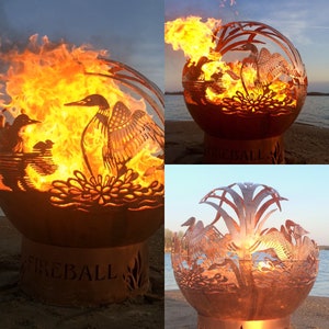 May include: A metal fire pit shaped like a sphere with a cut-out design of a loon and water plants. The fire pit is lit and has flames coming out of the top. The fire pit is sitting on a base with the word "FIREBALL" engraved on it.