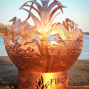 May include: A copper fire pit with a cut-out design of birds and plants. The fire pit has a round base with the words "BALL FIRE" inscribed on it.