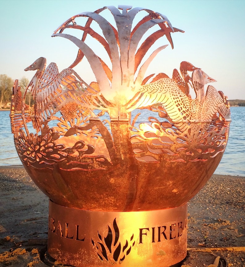 May include: A copper fire pit with a cut-out design of birds and plants. The fire pit has a round base with the words "BALL FIRE" inscribed on it.