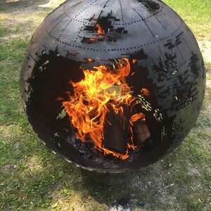 May include: A black metal sphere fire pit with a cut-out design. The fire pit is burning with orange flames inside.