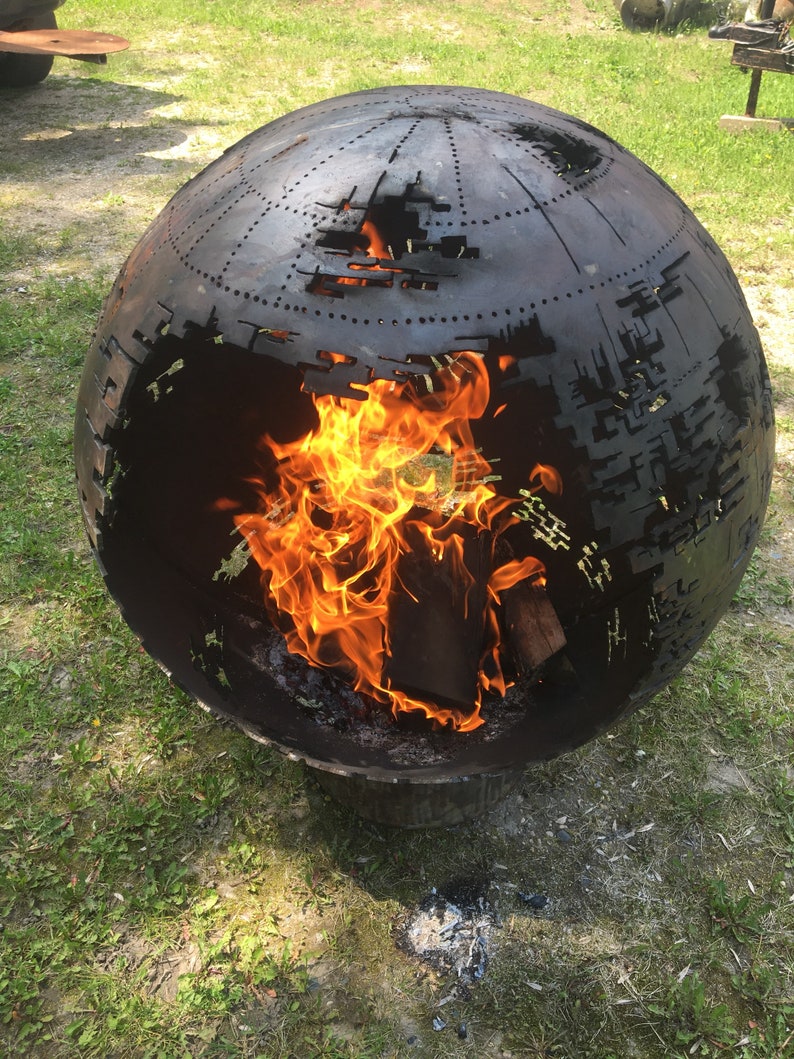 May include: A black metal sphere fire pit with a cut-out design. The fire pit is burning with orange flames inside.