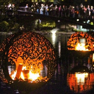 May include: Three decorative metal orbs with intricate cut-out designs, each containing a burning fire inside. The orbs are floating on a dark body of water, reflecting the flames.