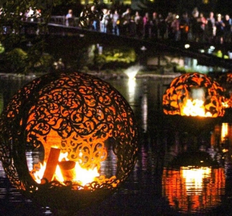 May include: Three decorative metal orbs with intricate cut-out designs, each containing a burning fire inside. The orbs are floating on a dark body of water, reflecting the flames.