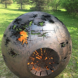 May include: A large, round, metal fire pit with a design resembling a planet. The fire pit is lit and the flames are visible through the cutouts in the metal.